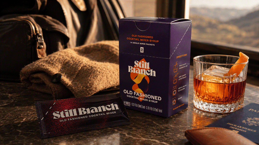 A single-serve cocktail mixer packet from Still Branch next to a rocks glass and a bottle of bourbon