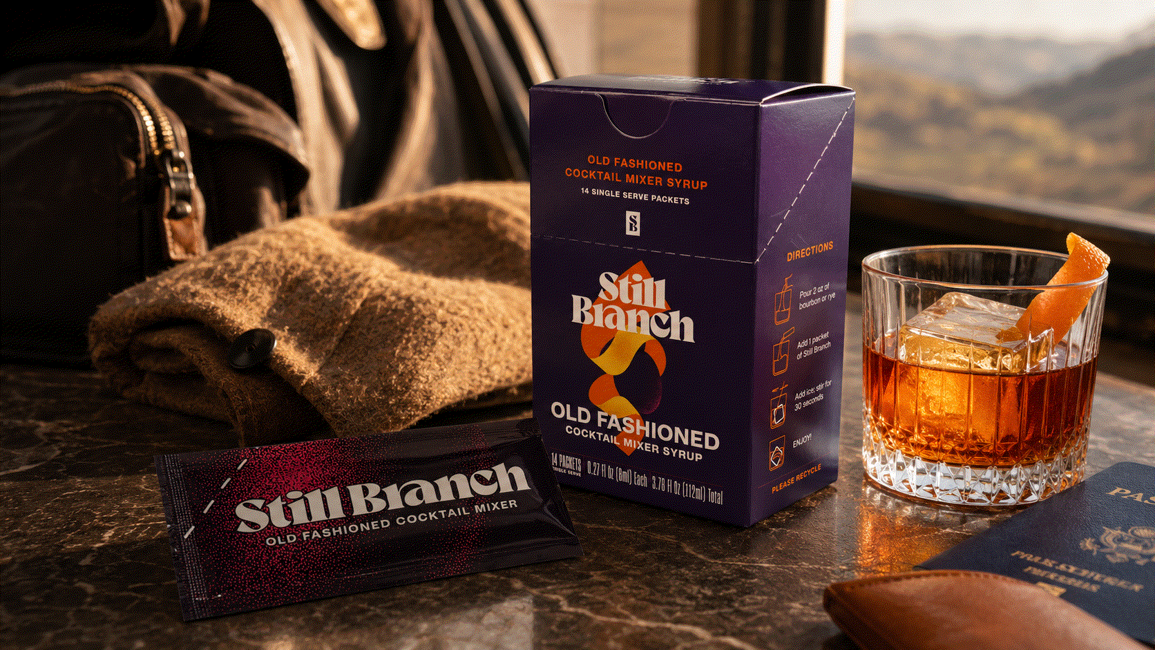 A single-serve cocktail mixer packet from Still Branch next to a rocks glass and a bottle of bourbon