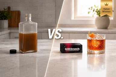 Comparison of a bottle of mixer syrup, Still Branch value winning packets, with an Old Fashioned cocktail on a counter.