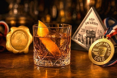 Old Fashioned Cocktail surrounded by award medals on a wooden surface.