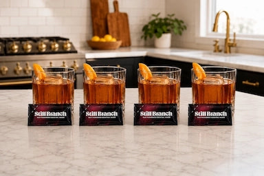 Four identical Old Fashioned Cocktails on a marble countertop with Still Branch packets.