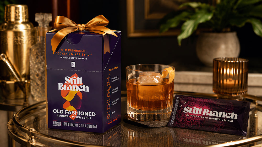 Still Branch Old Fashioned gift set box on a bar cart with a packet and a finished cocktail